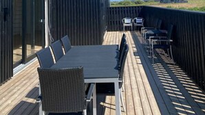 A covered outdoor deck with a dining table and chairs, a wicker sofa, and a view of the landscape.