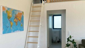 A staircase leading to a loft area with a wooden railing, a world map on the wall, a potted plant, and a grey sofa.