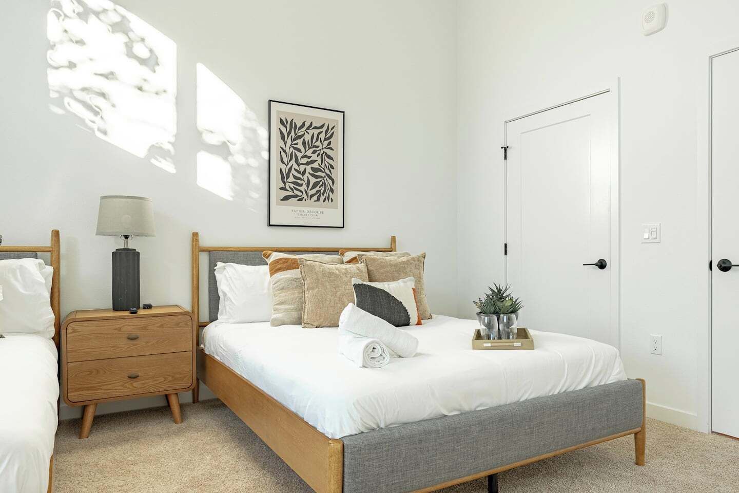 Een slaapkamer met een houten bed, een nachtkastje met een lamp, een kunstwerk in een lijst, en een deur.