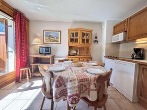 A cozy kitchen with a dining table set for four, a wooden cabinet, and a microwave. - 300m from ski lifts, 1st floor, balcony, tv, 25m², Praz sur Arly (Praz-sur-Arly)