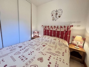 A bedroom with a bed, a nightstand, a lamp, a heart-shaped wall decoration, and a wardrobe. - 300m from ski lifts, 1st floor, balcony, tv, 25m², Praz sur Arly (Praz-sur-Arly)