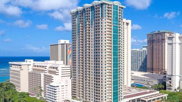 A high-rise hotel with multiple floors, a prominent blue accent on one side, and a view of the ocean. - Experience Island Paradise at The Grand Islander by Hilton - 2 Bd. Ocean View (Honolulu)