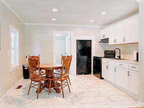A kitchen with white cabinets, a black refrigerator, and a dining table with chairs. - The Cypress Cottage - 2BR Beaufort Getaway - 10 min Downtown and Parris Island! (Beaufort)