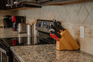 A kitchen with granite countertops, a stainless steel oven, and a knife block with red handles. - Go 13 Windsor AT Westside (Kissimmee)