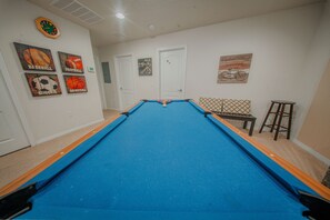A pool table in a room with a door, a bench, and wall decorations. - Go 13 Windsor AT Westside (Kissimmee)