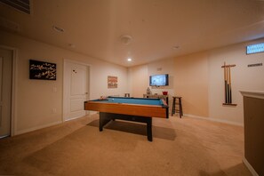 A pool table in a room with beige walls, a door, and a television mounted on the wall. - Go 13 Windsor AT Westside (Kissimmee)