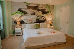 Een hotelkamer met een bed, een nachtkastje met een lamp, een muurschildering en een deur.