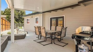 Eine überdachte Terrasse mit Tisch, Stühlen, einem Grill und einem Propangasbehälter.