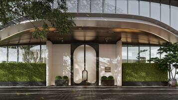 A modern building entrance with a curved overhang, glass doors, and a hedge.