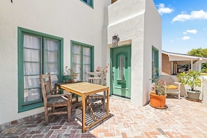 Eine Terrasse mit Holztisch und -stühlen, einer grünen Tür und Topfpflanzen.
