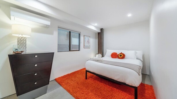 A modern bedroom with a bed, a dresser, and a window with blinds. - High Tide | Modern Design, Venice Energy (Los Angeles)