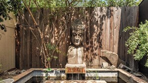 Un jardí amb una estàtua de Buda de pedra, un petit estany i una tanca de fusta.