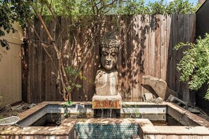 Ein Garten mit einer steinernen Buddha-Statue, einem kleinen Teich und einem Holzzaun.