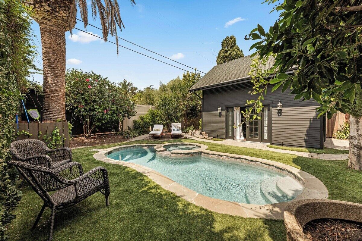 A backyard with a swimming pool, lounge chairs, a small hot tub, and a wooden deck.