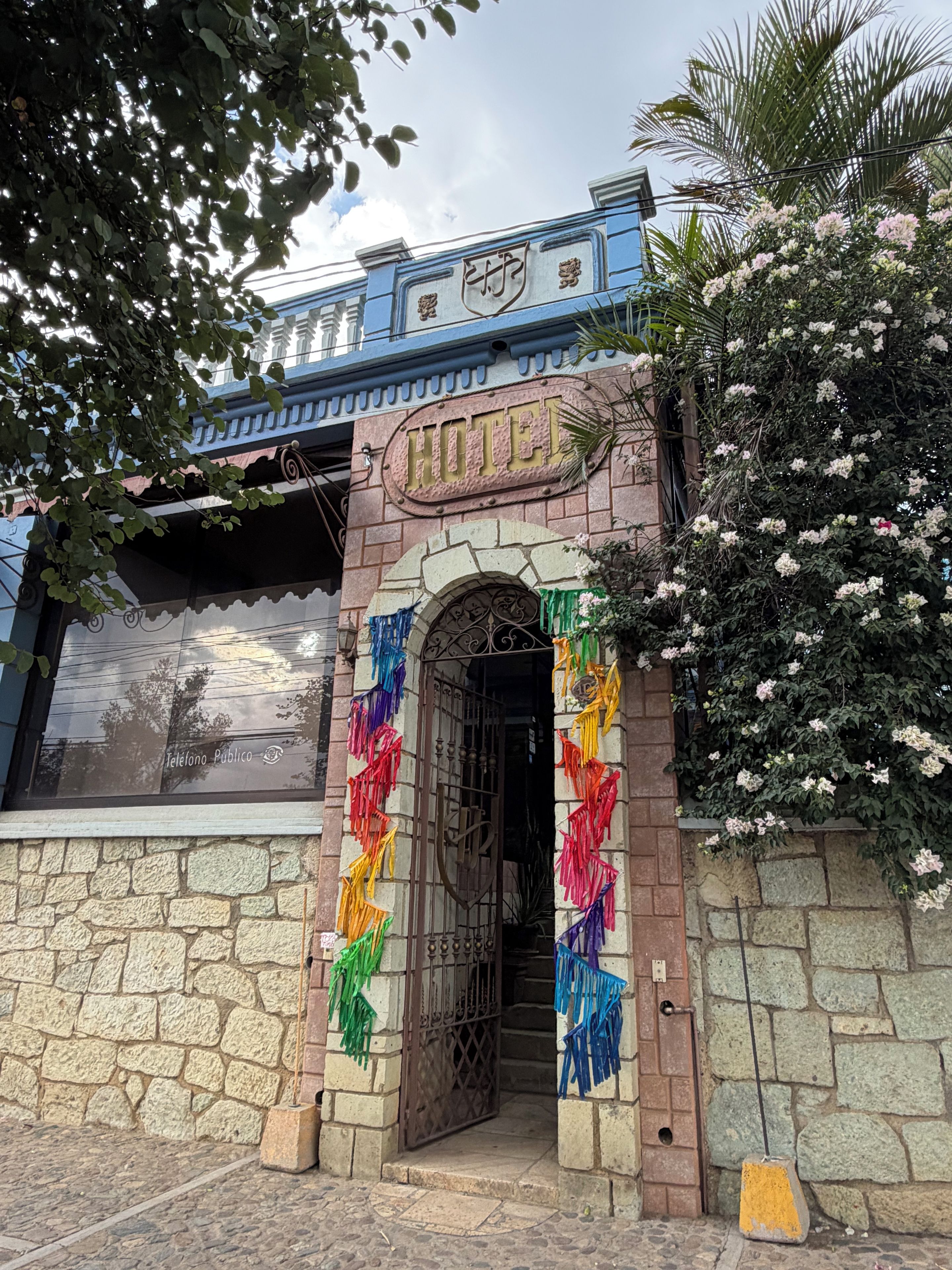 L’entrée d’un hôtel, avec une façade en pierre, un portail en métal et un panneau indiquant la présence de téléphones publics.