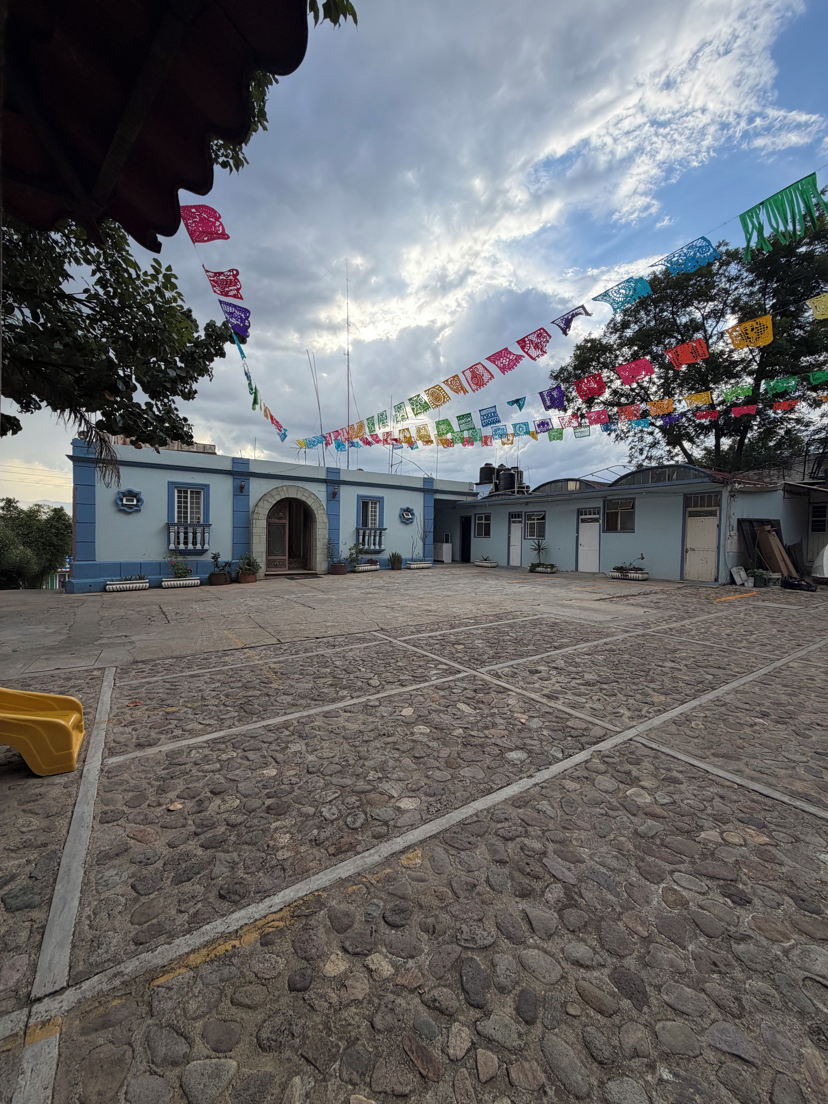 Un patio con suelo empedrado, un edificio de fachada azul y banderas de colores.