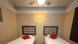 Ein Zimmer mit zwei Einzelbetten, einem Deckenventilator, einer Wandleuchte und einem gefliesten Boden.