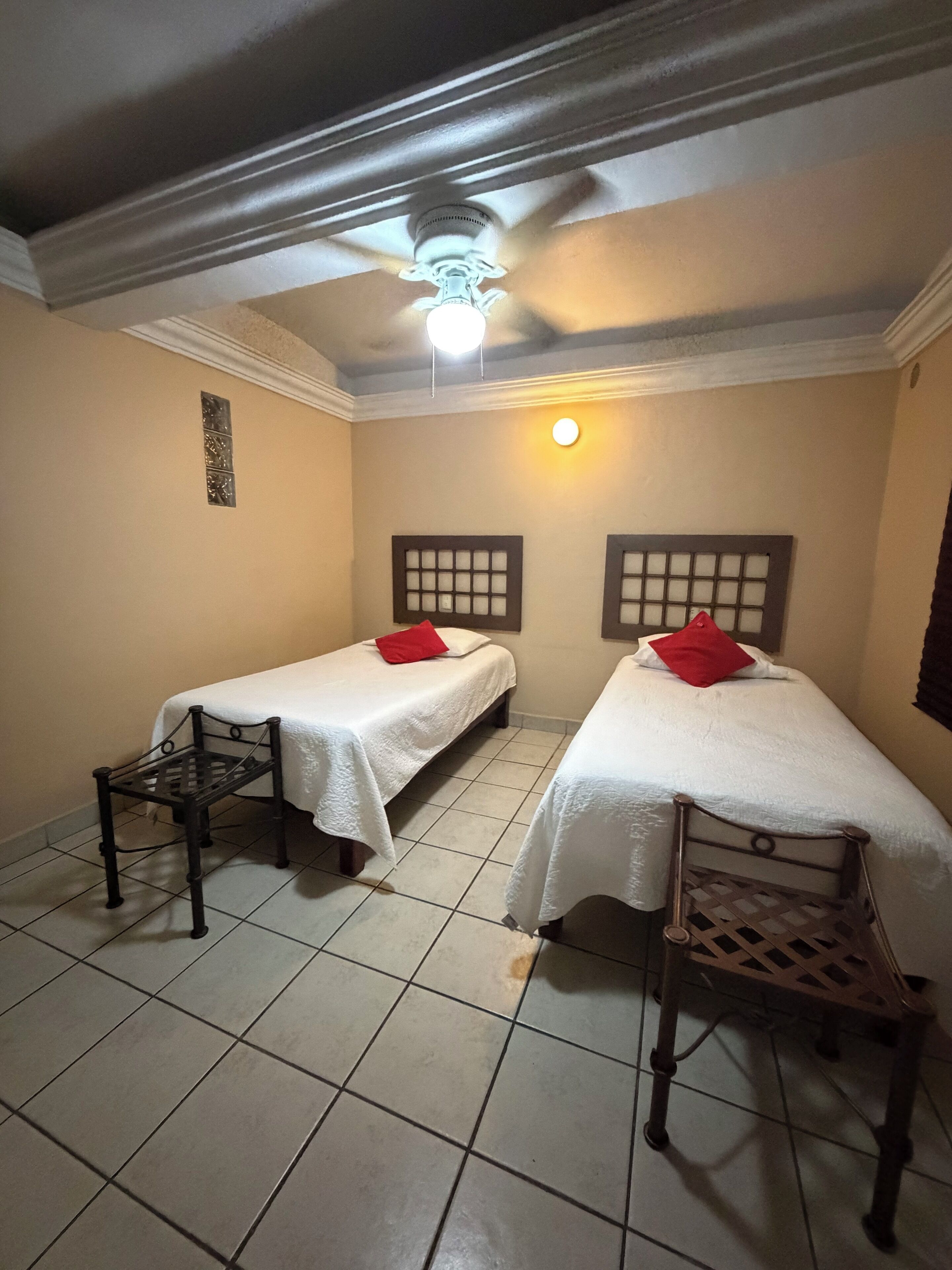 Quarto com duas camas de solteiro, cada uma com cabeceira e uma mesa pequena.