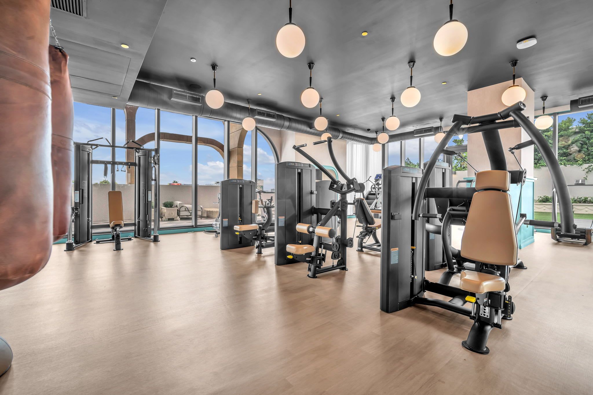 Une salle de sport équipée de divers appareils d’exercice, dotée de grandes fenêtres et d’un plancher en bois.