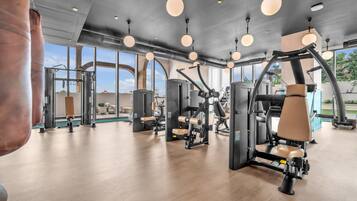 Une salle de sport équipée de divers appareils d’exercice, dotée de grandes fenêtres et d’un plancher en bois.
