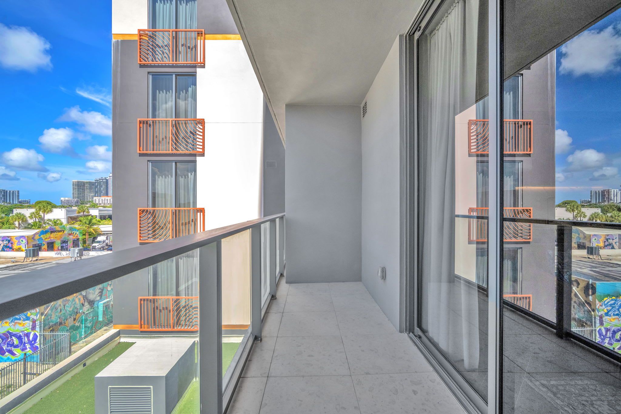 Un balcon offrant une vue dégagée sur le paysage urbain, avec des bâtiments modernes et une rue bordée de palmiers.