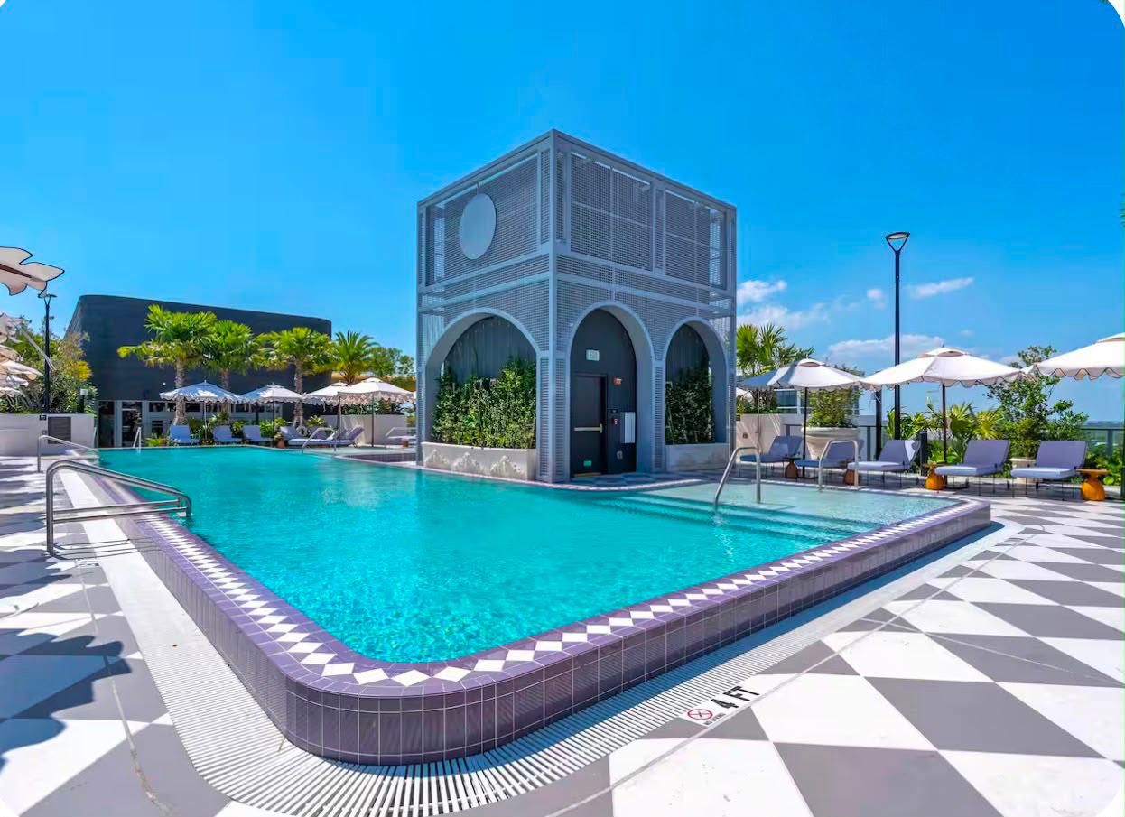 A swimming pool with a geometric building structure, sun loungers, and a tiled deck.