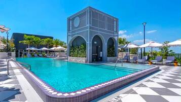 A swimming pool with a geometric building structure, sun loungers, and a tiled deck.