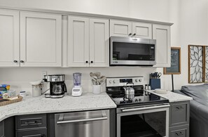 Eine moderne Küche mit weißen Schränken, einer Edelstahl-Mikrowelle, einer Kaffeemaschine, einem Mixer, einem Wasserkocher und einem Gasherd.