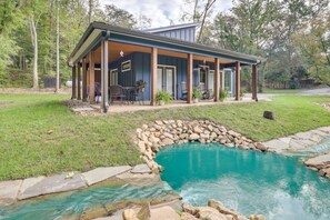 Ein Haus mit überdachter Terrasse, Swimmingpool und einem Wasserfall-Element aus Stein.