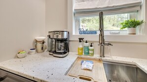 Una cocina con cafetera, lavamanos y ventana con vistas al verdor.