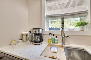 Eine Küche mit Kaffeemaschine, Spüle und Fenster mit Blick auf Grünflächen.