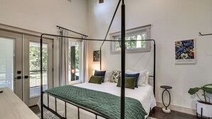 Una cama con dosel, con un edredón verde, una mesita de noche, una silla y una planta en maceta.