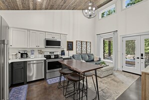 Eine moderne Küche mit weißen Schränken, Edelstahlgeräten und einem Essbereich mit Holztisch und Barhocker.
