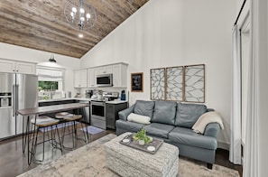 A modern kitchen with white cabinets, stainless steel appliances, and a dining area with a wooden table and metal chairs. - Whitewood Retreat w Hot Tub, Waterfall Views! (Wildwood)