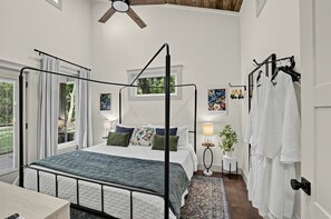 Ein Bett mit Baldachin, ein Nachttisch mit Lampe und ein an der Wand befestigter Kleiderhaken mit aufgehängter Kleidung.
