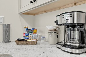 Una cocina con cafetera, una cesta de comestibles y un tarro etiquetado 'SWEET'.