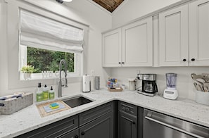 A modern kitchen with white cabinets, a stainless steel dishwasher, a coffee maker, and a blender. - Whitewood Retreat w Hot Tub, Waterfall Views! (Wildwood)