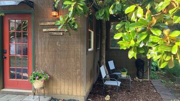 A wooden building with a red door, a sign that reads 'HOME OF SWEETNESS TO YOU,' and a potted plant with pink flowers.