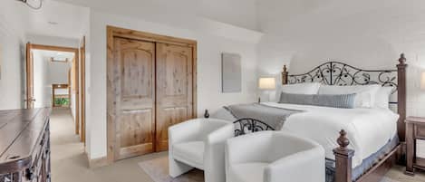 A bedroom with a bed, two chairs, a wooden wardrobe, a ceiling fan, and a TV.
