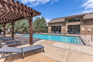 A pool area with lounge chairs, a covered seating area, and a building with a pool entrance. - Park City Retreat | A/C + Hot Tub + Shared Pool (Park City)