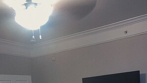 Makuuhuone, jossa on sänky, ovi, seinälle asennettu televisio ja kattovalaisin.