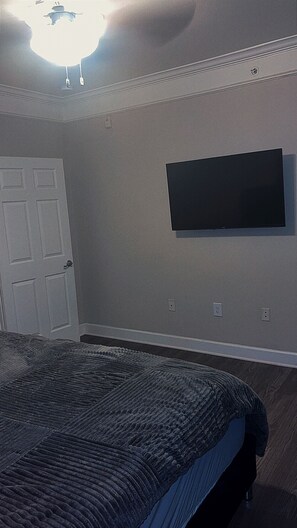 Ein Schlafzimmer mit einem Bett, einer Tür, einem an der Wand befestigten Fernseher und einer Deckenleuchte.