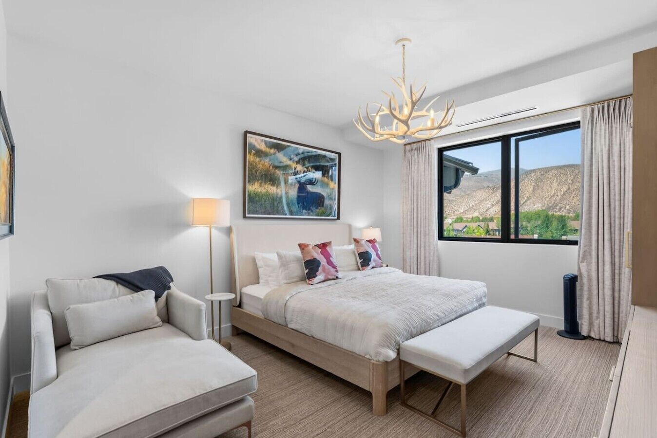 A modern bedroom with a large bed, a bedside table, a chair, a floor lamp, and a window with a view.