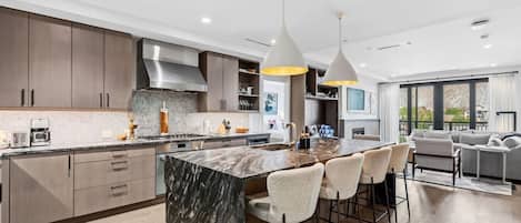 A modern kitchen with a marble island, bar stools, and pendant lighting.