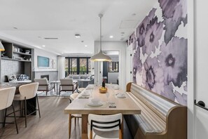 A modern dining area with a wooden table, white chairs, and a bench. There is a large window providing natural light and a view of the outdoors. - Frontgate | Luxury Condo W/Resort Amenities (Avon)