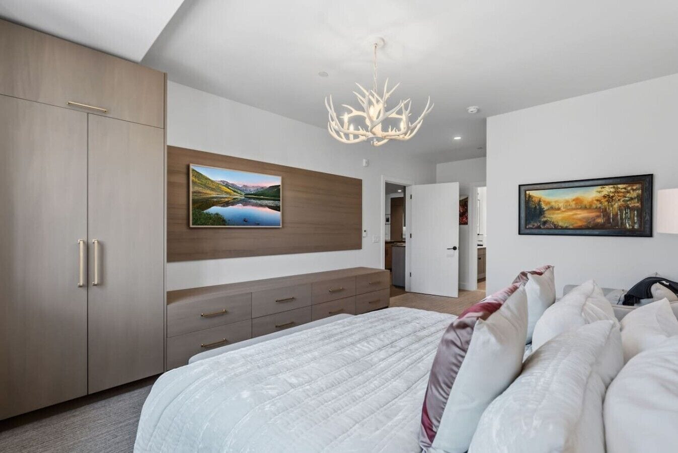 A modern bedroom with a large bed, a wardrobe, a desk, and two wall-mounted paintings.