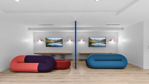 Ein modernes Zimmer mit Holzboden, zwei Sitzsäcken, einer zentralen Säule und zwei an der Wand befestigten Fernsehern, die Landschaftsbilder zeigen.