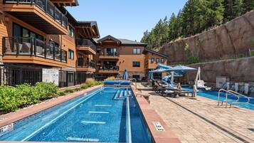 A swimming pool area with a multi-level building, lounge chairs, and a slide.