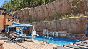 Ein Schwimmbad mit Rutsche, Liegestühlen und einem Holzgebäude im Hintergrund.