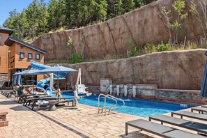 A swimming pool with a slide, lounge chairs, and a wooden building in the background. - Frontgate | Luxury Condo W/Resort Amenities (Avon)